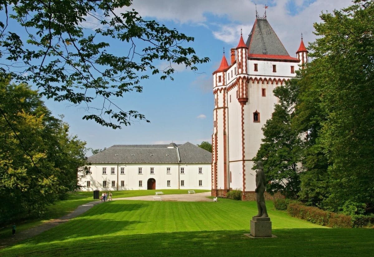 Bílý zámek v Hradci nad Moravicí s bílo-červenou věží nad zámeckým trávníkem